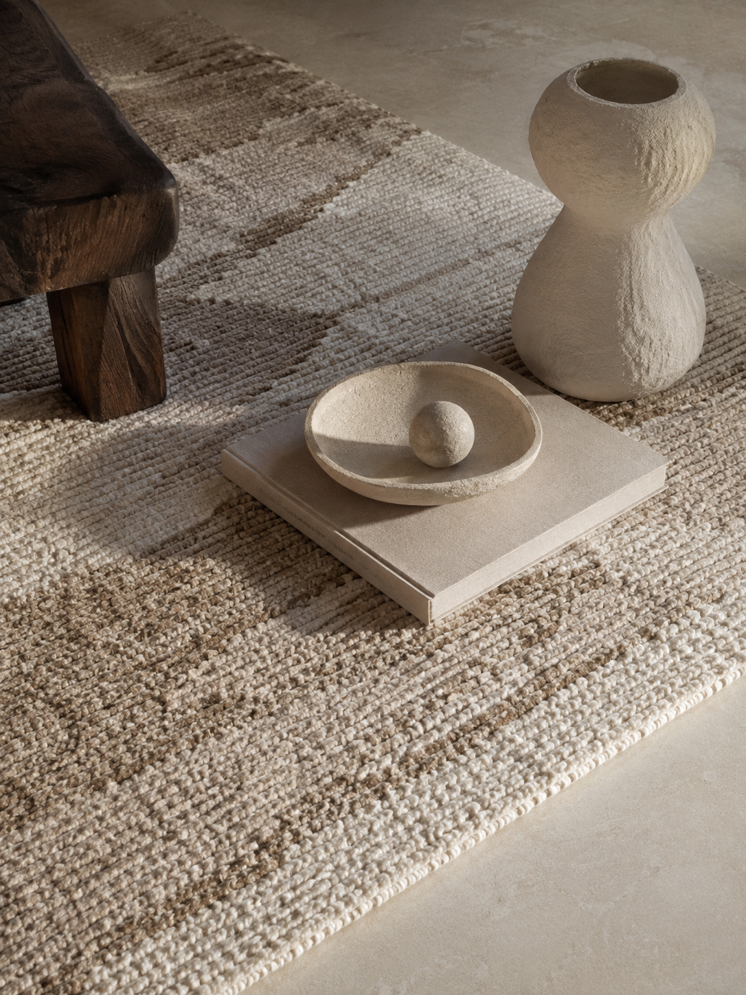 A ceramic vessel, a stone bowl and a book resting on a woven wool rug