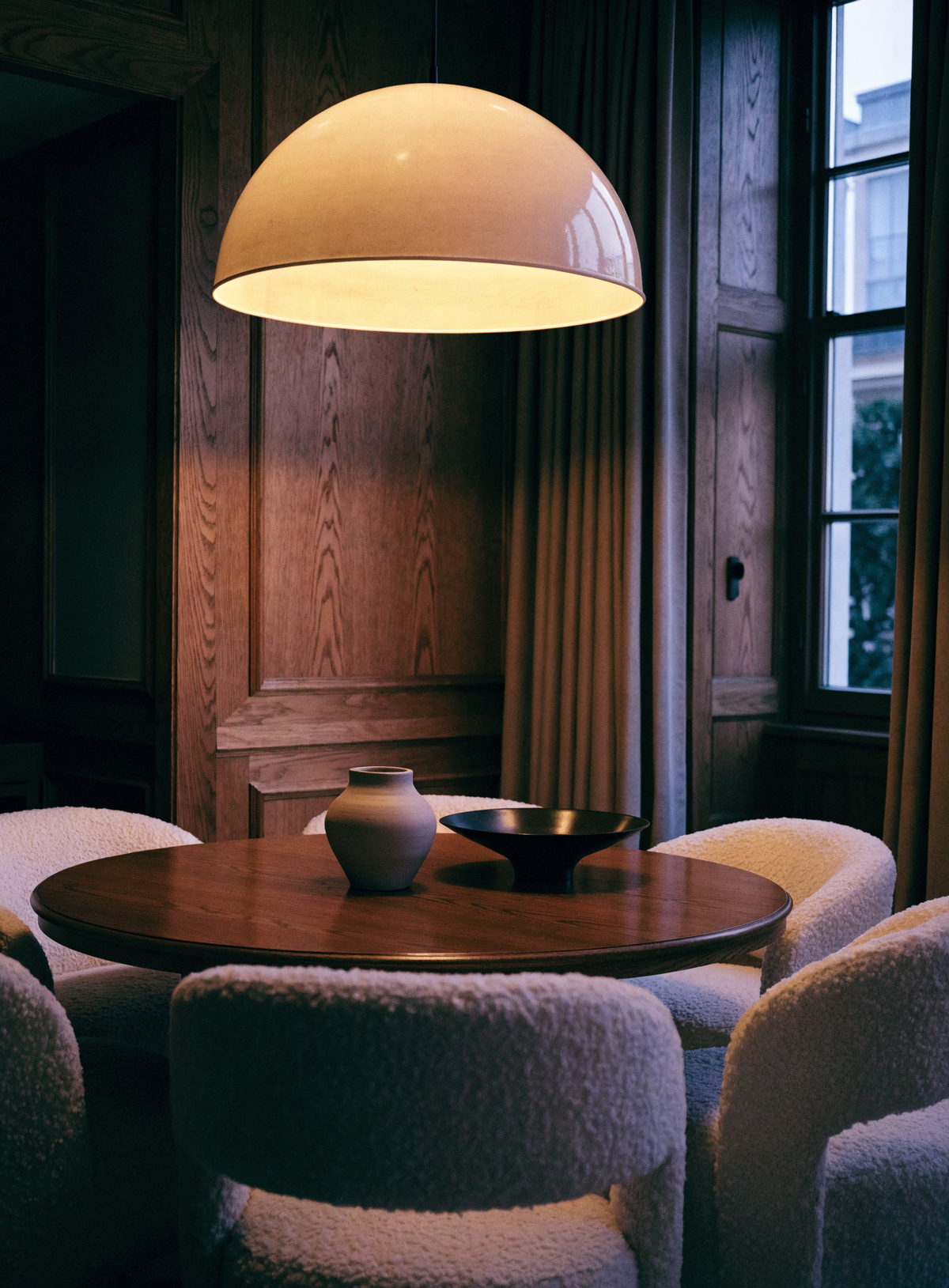 Round dark oak dining table with boucle chairs under a pale pendant lamp
