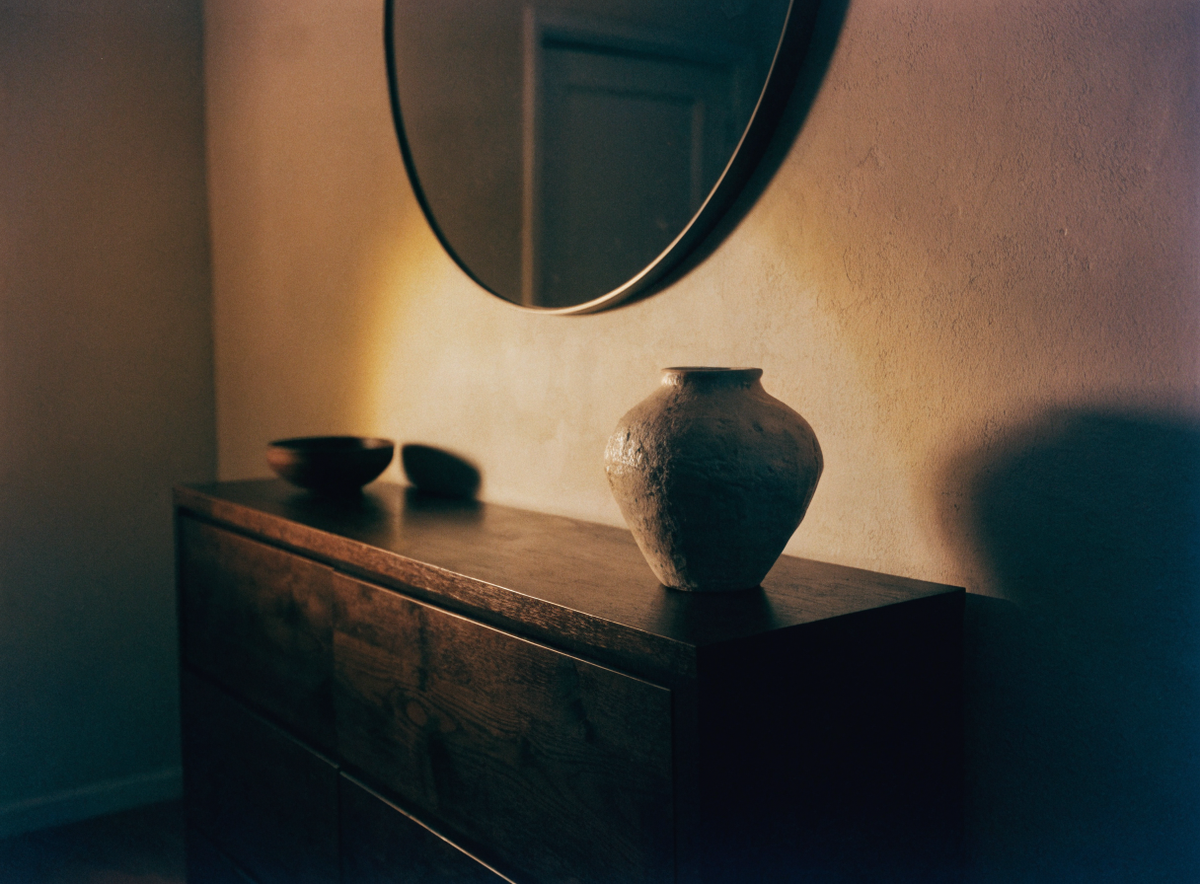 Round mirror above a dark wood sideboard in warm wall light